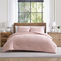 a bed with pink comforter and pillows in front of a window