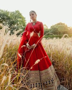 a woman in a long red dress standing in tall grass with her hands on her hips