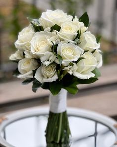 a bouquet of white roses sitting on top of a glass table next to a plate