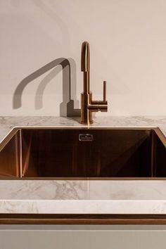 a kitchen sink with a faucet and marble counter top in front of a white wall