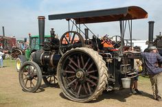 an old fashioned tractor is parked on the grass with people standing around and looking at it