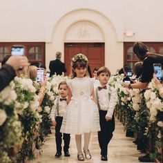 two young children are walking down the aisle with flowers in their hair as people take pictures