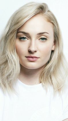 a woman with blonde hair and blue eyes wearing a white t - shirt is looking at the camera