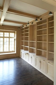 an empty room with wooden bookshelves and windows in the wall, along with hardwood flooring