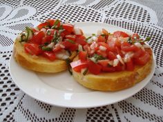 two pieces of bread with tomatoes and onions on it sitting on a tablecloth covered table