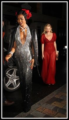 two women dressed in silver and red walking down the street with one wearing a black jacket