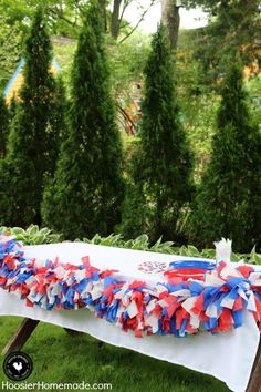 a table with red, white and blue streamers on it in front of trees