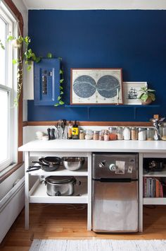 a kitchen with blue walls and white counter tops, pots and pans on the shelves