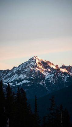 the mountains are covered in snow and trees as the sun is setting on top of them