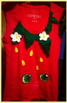 a red shirt with green eyes and white flowers on the front is hanging from a rack