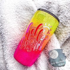 a pink and yellow glitter tumbler sitting on top of a pile of white blankets