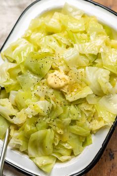 a white plate topped with cabbage covered in butter and seasoning next to a fork