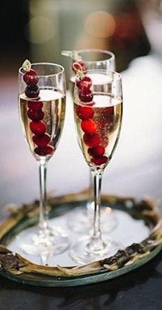 two glasses of wine on a tray with berries in the glass and one filled with champagne