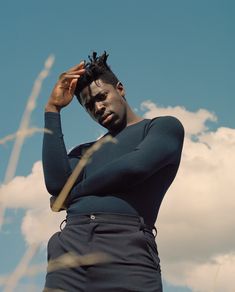 a man with dreadlocks on his head standing in front of some tall grass