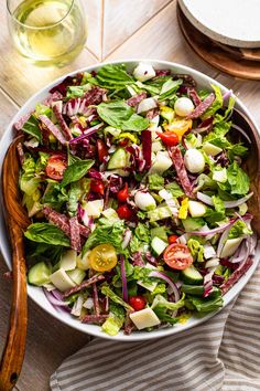 a salad with lettuce, tomatoes and onions in a white bowl on a wooden table