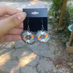 a pair of earrings that have been made out of pixelated glass beads and are being held in front of a card