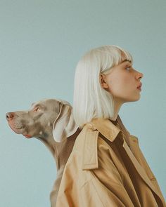 a woman in a trench coat with a dog on her back, looking up at the sky