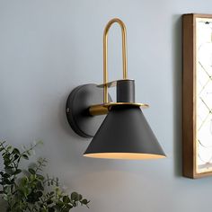 a black and gold wall light next to a potted plant