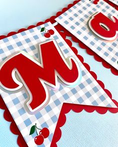 two red and white paper banners with the letter m on them, one has cherries