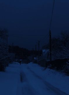 a dark street with snow on the ground and power lines in the distance at night