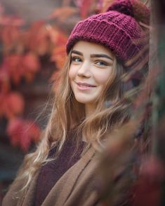 a woman with long hair wearing a purple knitted hat and brown coat looking at the camera