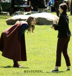 a woman in a cape is talking to another woman on the grass with other people behind her