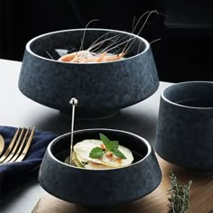 three black bowls with food in them on a wooden board next to silverware and utensils