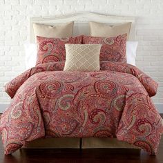 a bed with red and tan comforters in front of a white brick wall