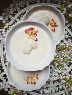 two white bowls filled with soup on top of a doily next to pink and yellow flowers