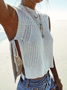 a woman standing on top of a sandy beach holding her hand up to the side