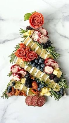 a christmas tree made out of cheeses and fruits on a marble counter top with greenery