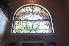 an arched window with iron work on the outside and inside, above a doorway in a home