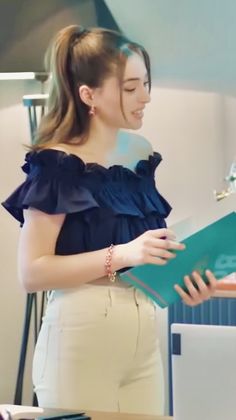 a woman standing in front of a laptop computer holding a folder and looking at it