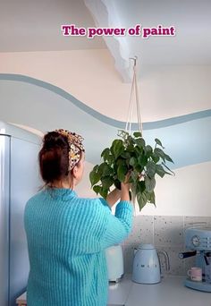 a woman is holding a potted plant in the air and looking up at it