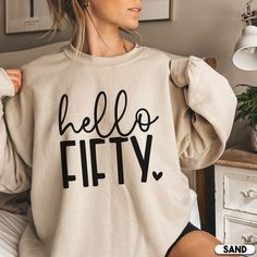 a woman wearing a sweatshirt with the words hello fifty printed on it in black ink