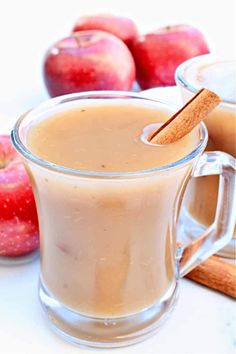 an apple cider with cinnamon stick in it next to two glasses filled with apples