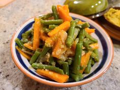 a bowl filled with green beans and carrots on top of a marble countertop