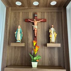 three wooden crucifixs with flowers in a vase on the shelf next to them