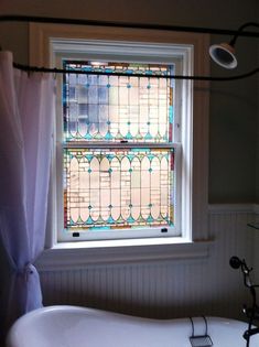 a bath tub sitting under a window next to a white sink in a bathroom below a stained glass window