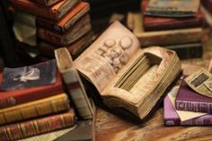 an open book sitting on top of a wooden table next to stacks of old books