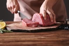 a person cutting up meat on top of a wooden cutting board next to lemon wedges