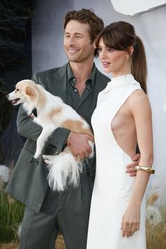 a man and woman standing next to each other holding a dog