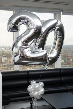 silver balloons in the shape of two are attached to a table with a black bench