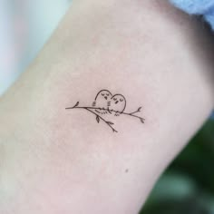 a small tattoo on the back of a woman's left arm shows two birds sitting on a branch