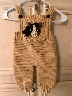 a crocheted baby's overall with a teddy bear on it hanging from a hook