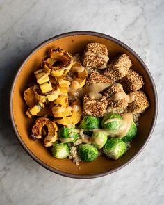 a bowl filled with broccoli, cauliflower and other foods on top of a marble table