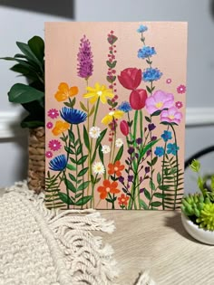 a card with flowers painted on it next to a potted plant