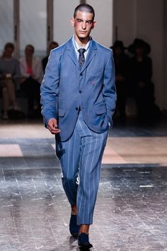 a man in a suit and tie walks down the runway