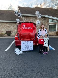 a woman and two children standing in front of a red car with dalmatian print on it