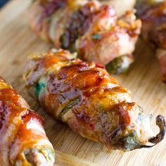 several pieces of meat wrapped in bacon on a wooden cutting board with dipping sauces